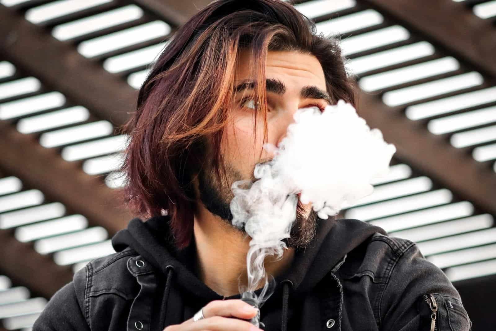 what is vaping in dubai - Close-up of a stylish man vaping outdoors, creating thick vapor clouds.